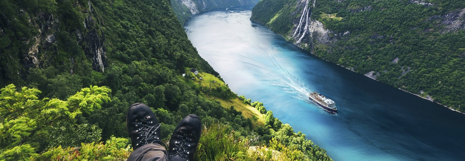 Person sitting on mountain overlooking fjords and a Havila cruise ship